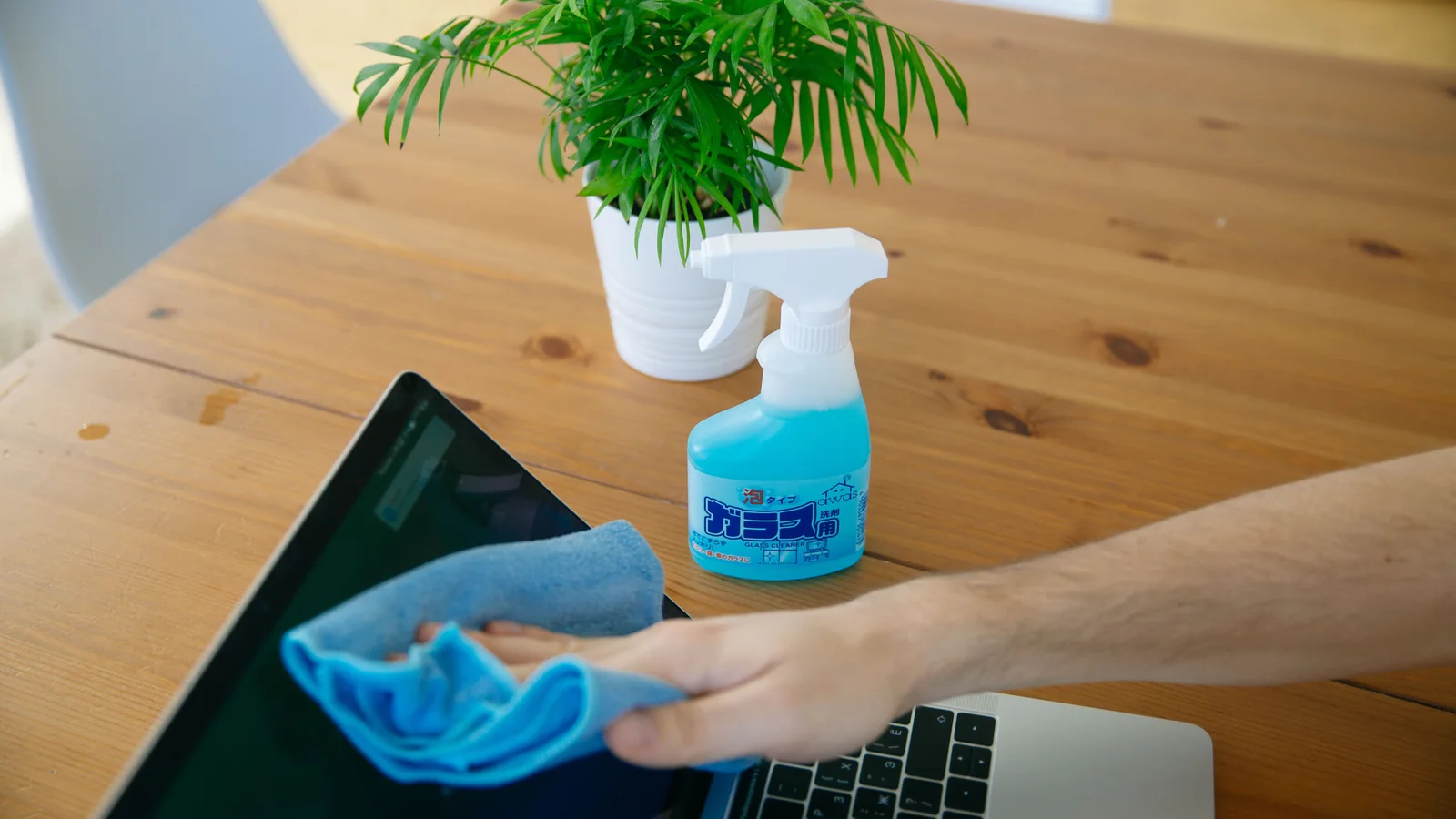 Hand reinigt einen Laptopbildschirm an einem Arbeitsplatz mit einem Mikrofasertuch