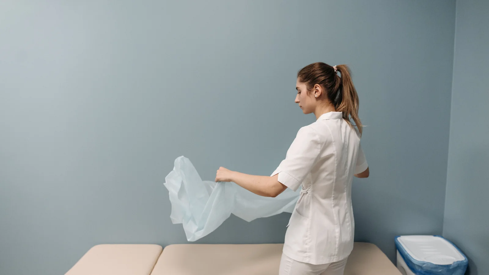 Behandlungsliege in einem Praxisraum wird hygienisch mit einer frischen Auflage vorbereitet